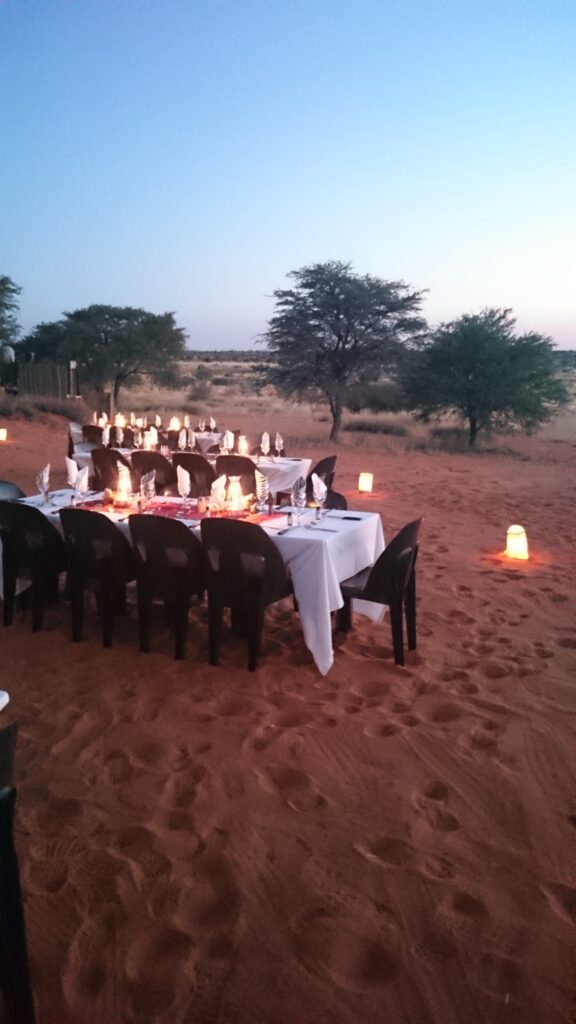 Candle-Light-Dinner im Busch mit gedeckten Tischen auf rotem Sand in Südafrika