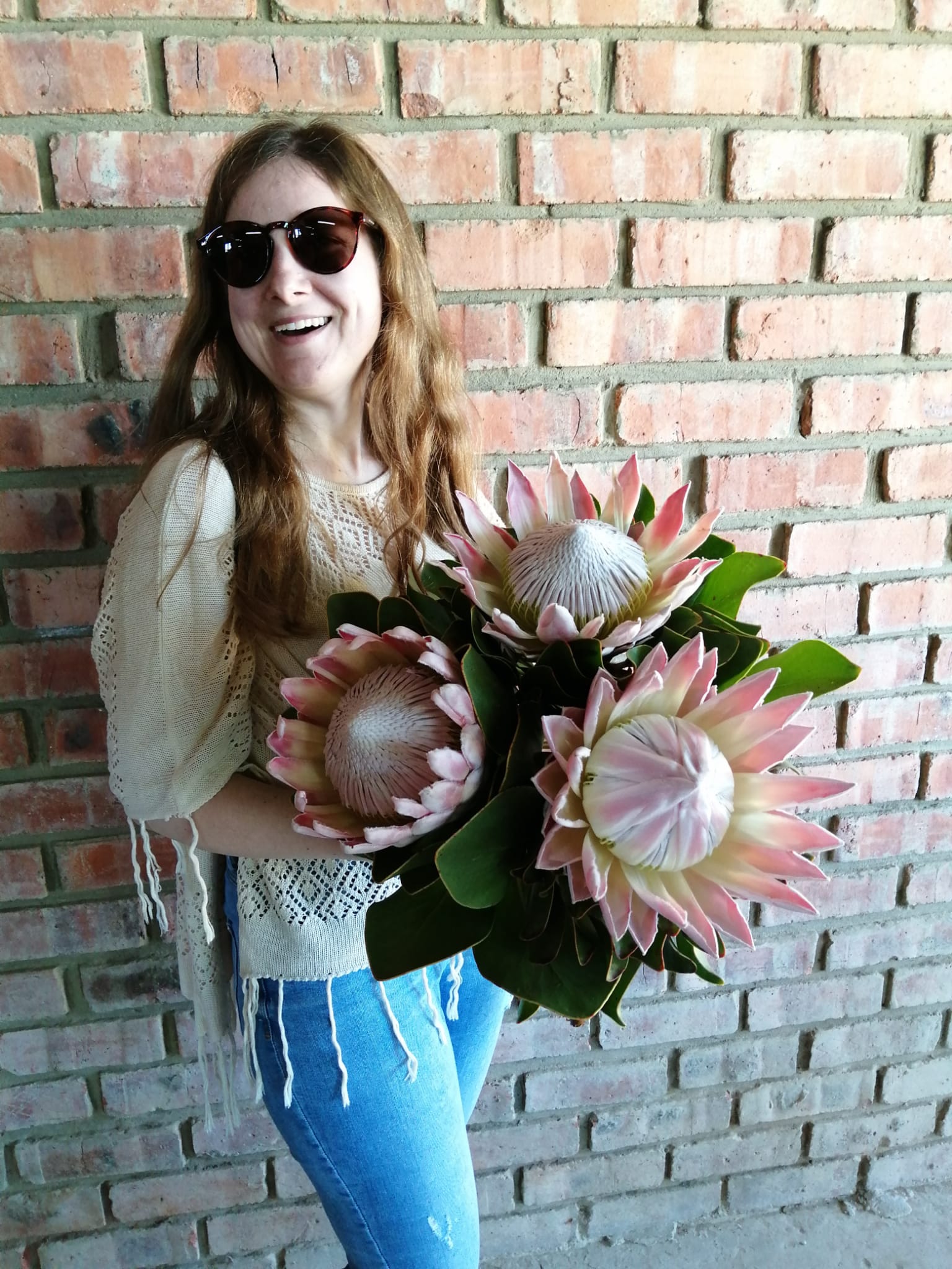 Frau mit Protea-Blumen vor Backsteinwand