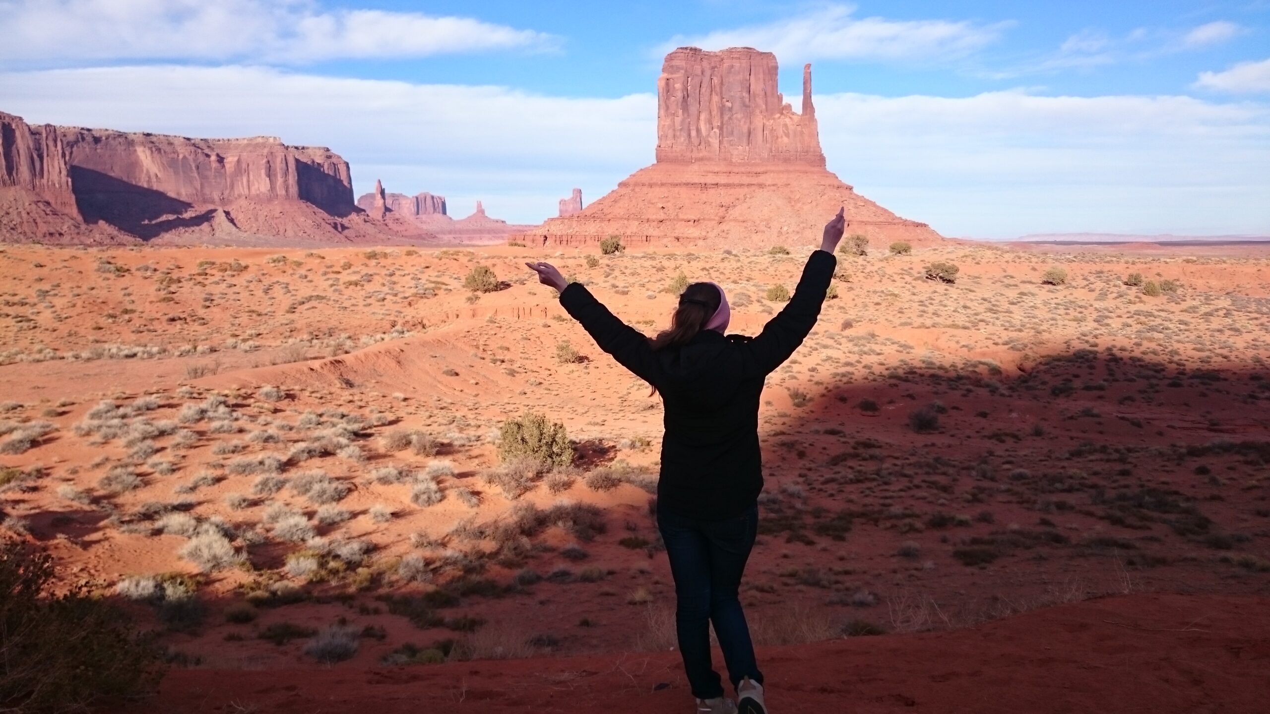 Reisende (Larissa) mit erhobenen Armen vor Felsformation im Monument Valley, Utah