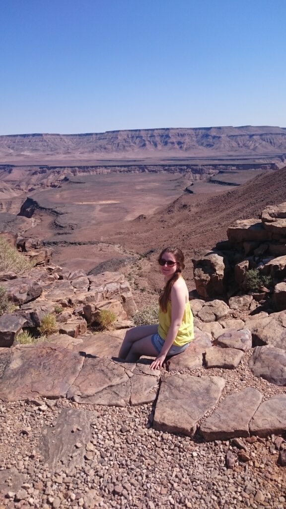 Larissa Wolfram-Kuhl sitzt auf Felsen mit Blick über weite Canyonlandschaft