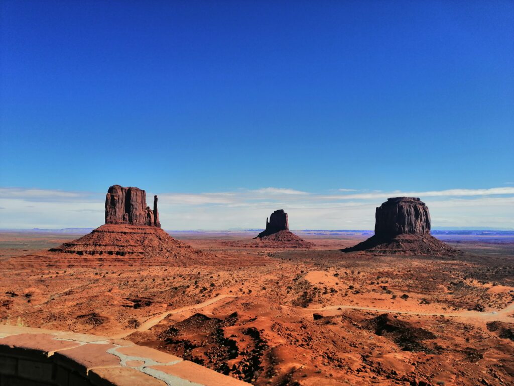 Das atemberaubende Monument Valley im strahlenden Sonnenschein – beeindruckende rote Felsformationen, die die Weite und Schönheit der amerikanischen Wüste eindrucksvoll präsentieren. Ein unvergessliches Naturhighlight für deinen Traumurlaub.