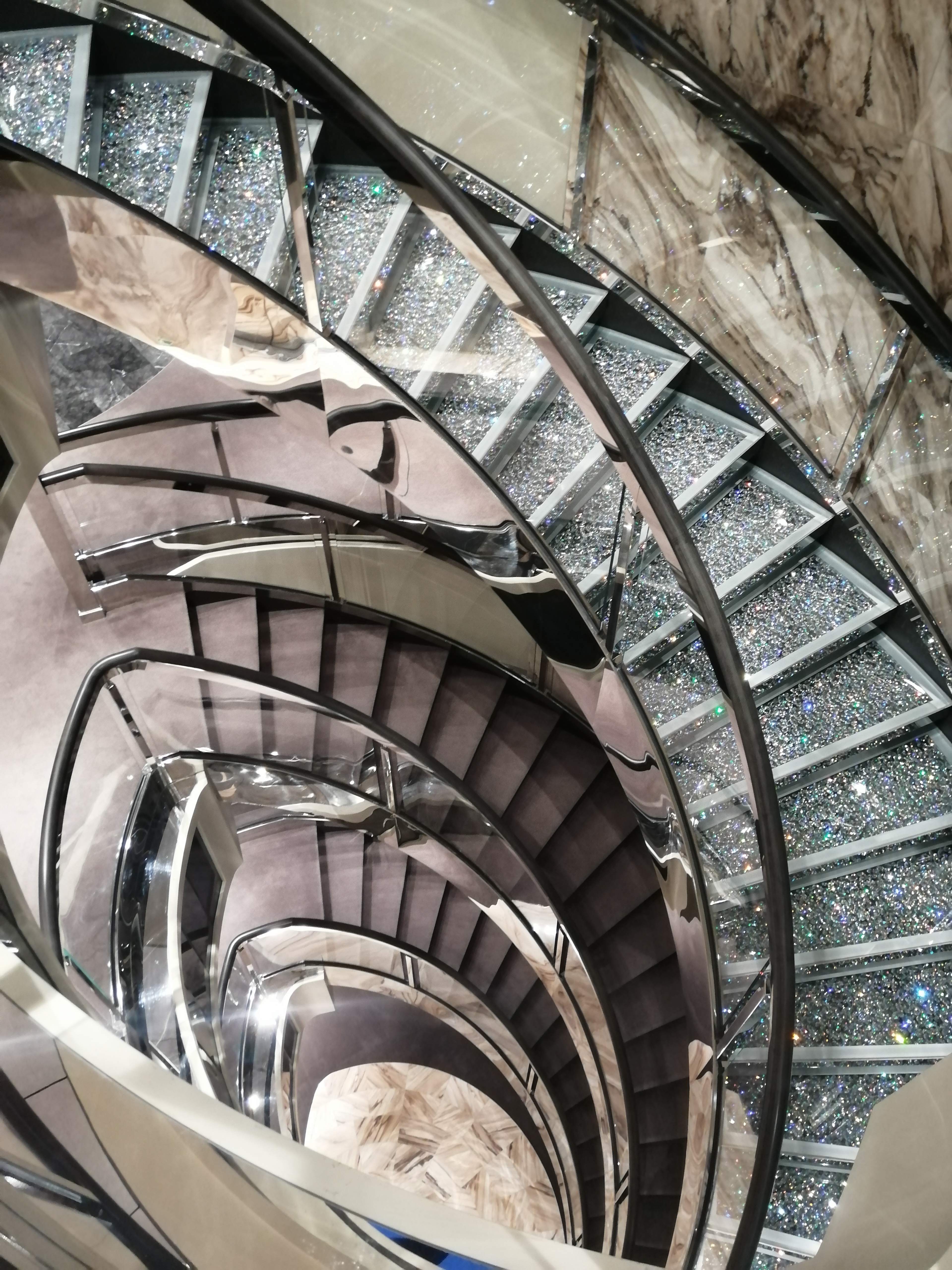 Geschwungene Treppe mit Glasgeländer im Atrium eines Kreuzfahrtschiffs