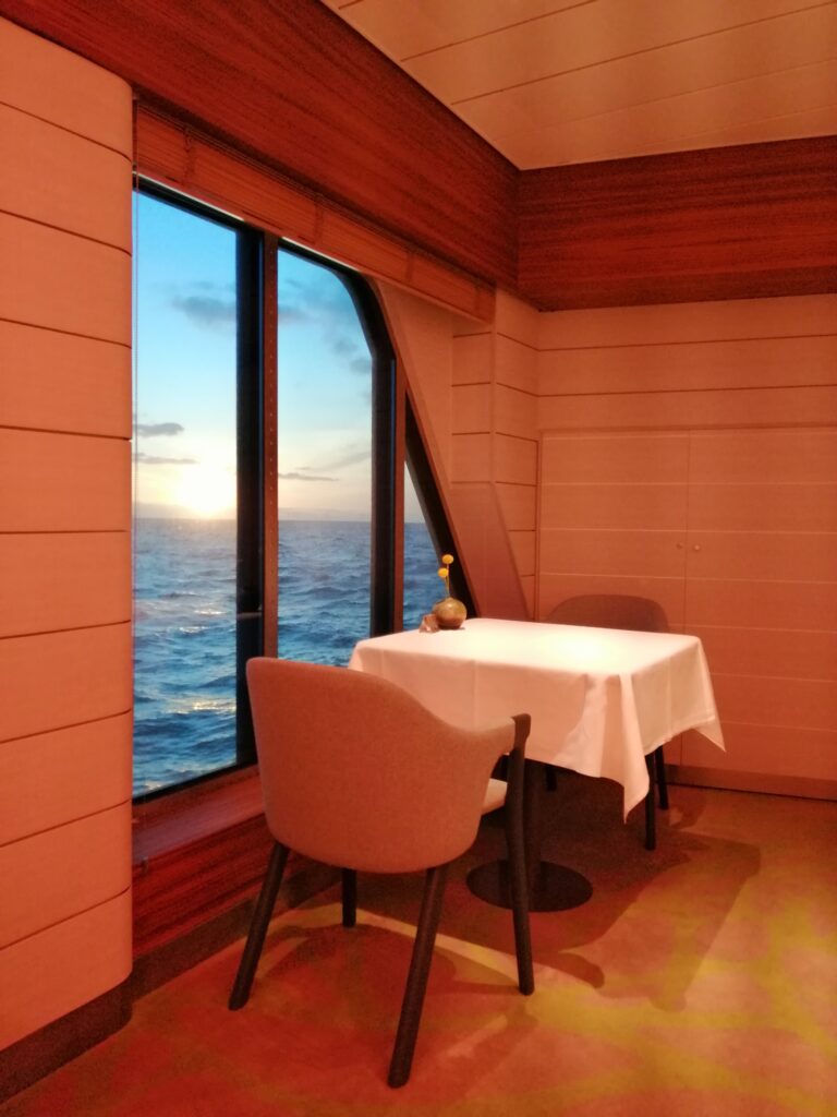 Restaurant auf Kreuzfahrtschiff mit Meerblick durch Panoramafenster bei Sonnenuntergang