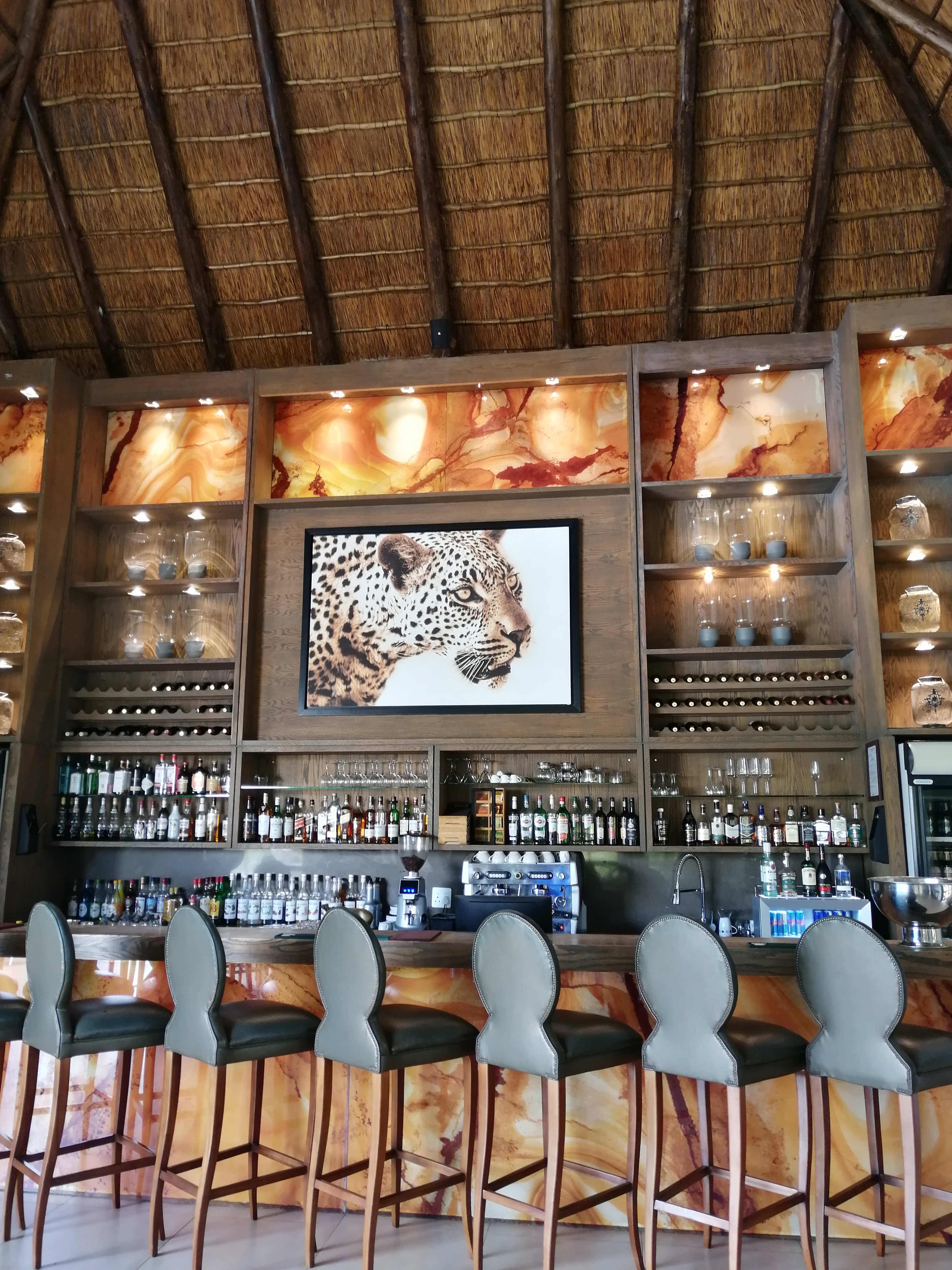 Safari-Lodge-Bar mit Strohdach, Holztresen und Tierkunst in Südafrika