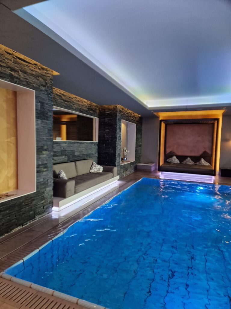 Indoorpool, Wellnessbereich, Design Couch, Kissen, Luxuriöser Innenpool mit Steinwänden und indirekter Beleuchtung