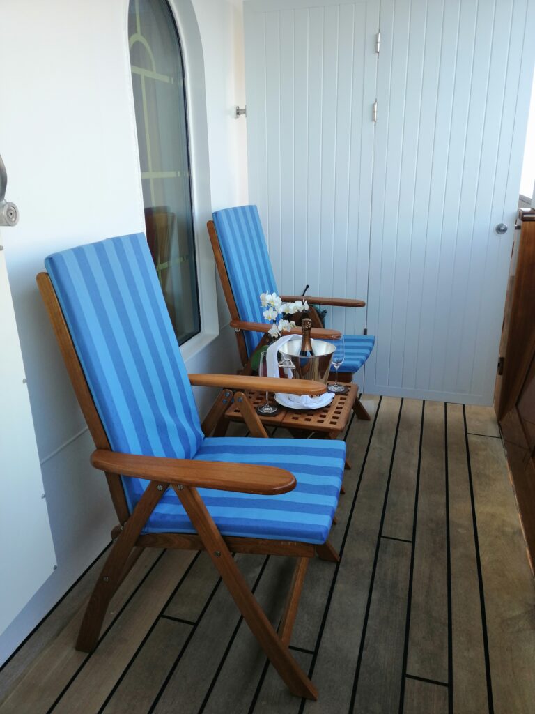 Zwei Stühle mit Holzboden und Sitzauflagen auf Balkon eines Kreuzfahrtschiffes