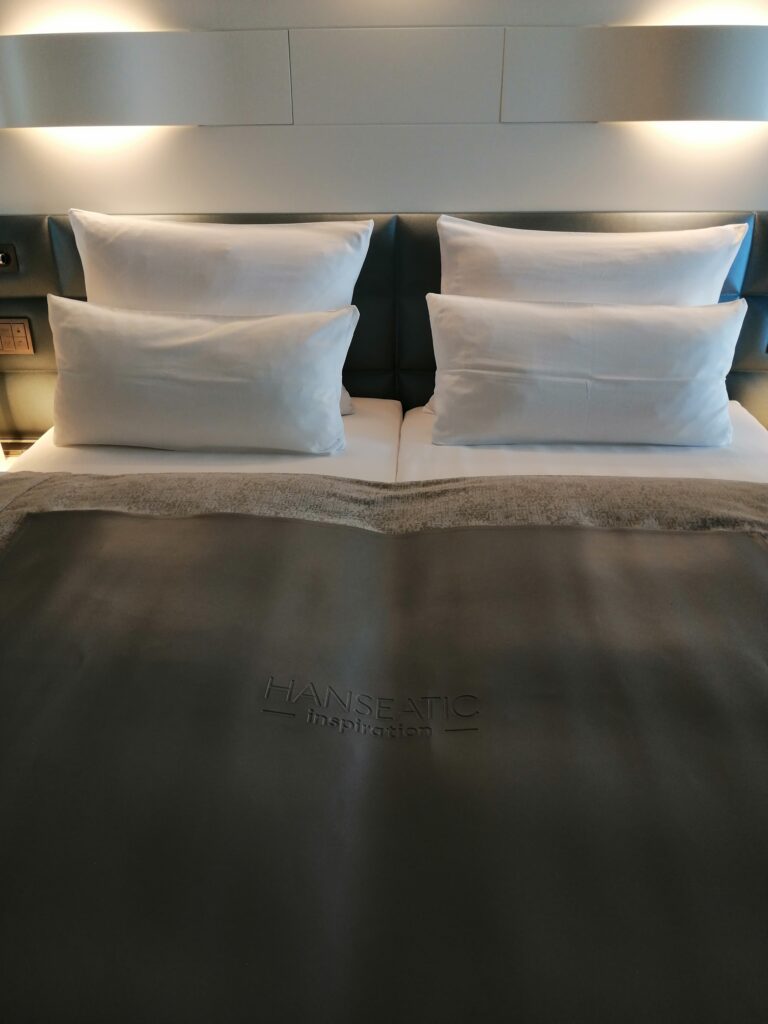 Kingsize Bett auf hochwertigem Kreuzfahrtschiff mit weißen Kissen und grauer Decke