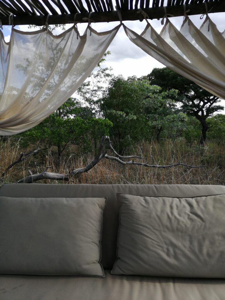 Blick auf ein Sofa mit zwei sofakissen vor offener Natur mit Moskitonetz darüber