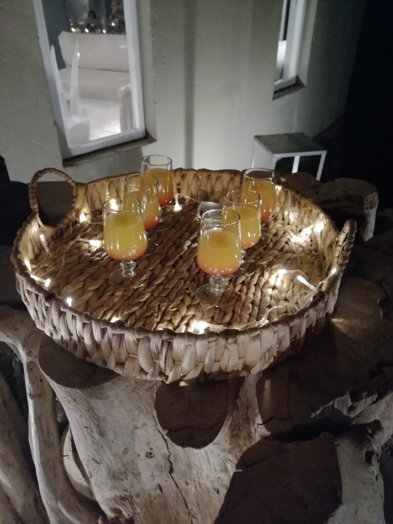 Sundowner werden auf Tablett mit Lichterkette hochwertig serviert, Tablett mit Gläsern und Saft auf dekorativem Holztisch